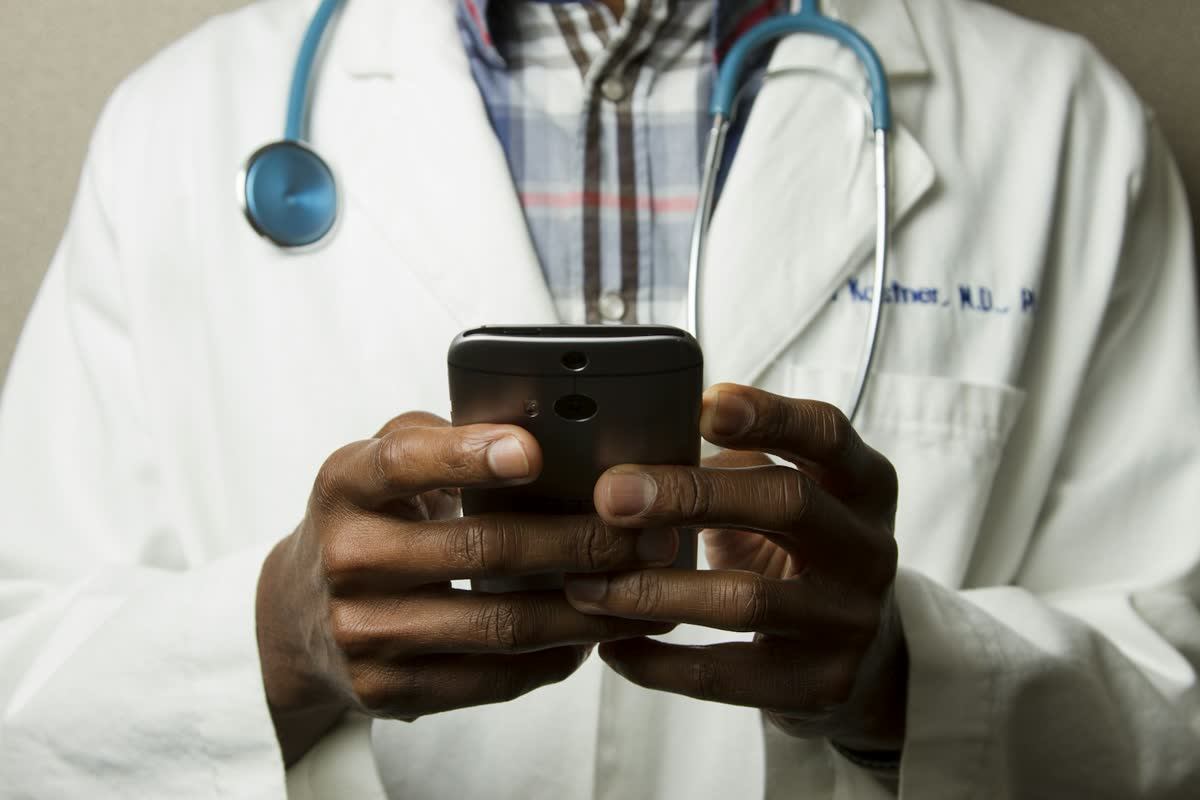 A clinician in a white coat checking a phone
